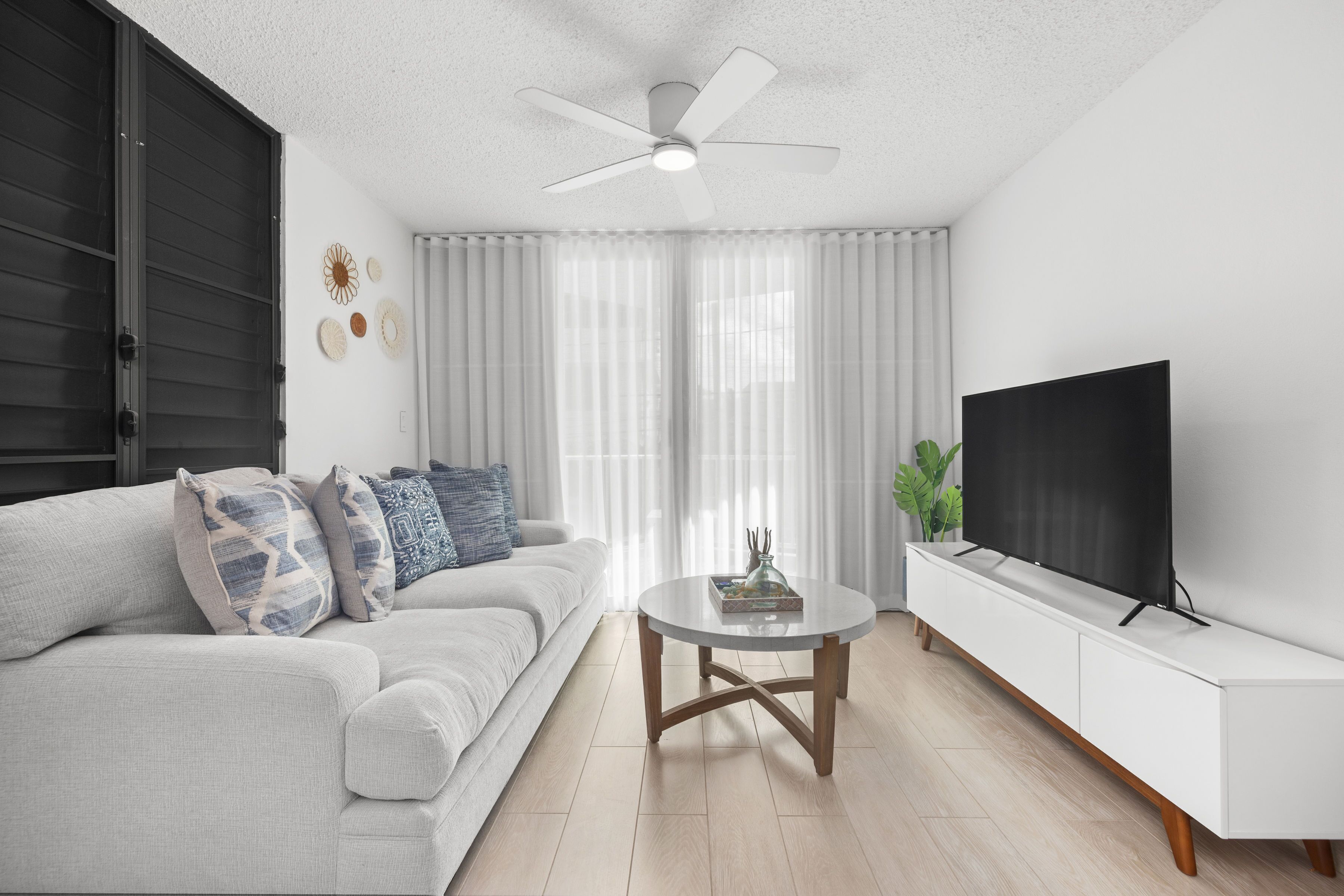 Ein modernes Wohnzimmer mit Sofa, Couchtisch, Fernseher und Deckenventilator.