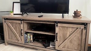 A wooden entertainment center with a flat-screen TV, a framed menu, and a small plant. - Cozy cabin in charming Cypress Hills with WiFi (Cypress County)