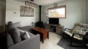 A living room with a sofa, coffee table, TV, and a fireplace. - Cozy cabin in charming Cypress Hills with WiFi (Cypress County)