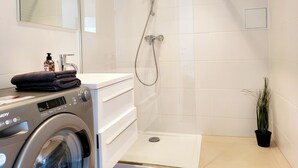 A modern bathroom with a washing machine, a shower, and a potted plant.