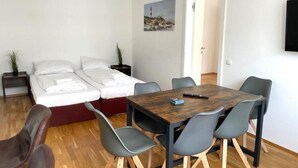 A modern room with a bed, a dining table, and chairs. There is a painting on the wall and a TV mounted on the wall.