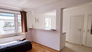 A room with a bed, a window with curtains, a shelf with a picture, and a door.