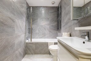 A modern bathroom with a glass shower enclosure, a bathtub, and a sink with a mirror above it. - Elegant 2BD Flat 5 Mins to Kensington Gardens! (London)