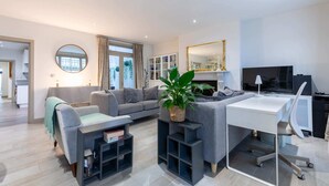 A modern living room with a grey sofa, a white desk, and a large mirror. - Elegant 2BD Flat 5 Mins to Kensington Gardens! (London)