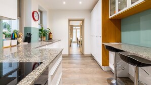 A modern kitchen with granite countertops, a built-in stove, and a bar area with stools. - Elegant 2BD Flat 5 Mins to Kensington Gardens! (London)