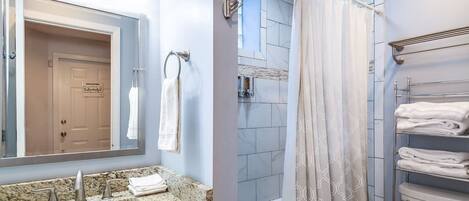 Un baño con lavamanos de granito, espejo, ducha con cortina estampada y inodoro con toallero.