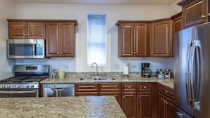 Una cocina con encimeras de granito, electrodomésticos de acero inoxidable, armarios de madera y un ventanal con persianas.
