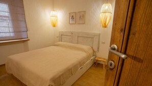 A bedroom with a bed, wooden floor, a door, and two wall-mounted lamps. - Le Scalette Apartment - G (Osimo)