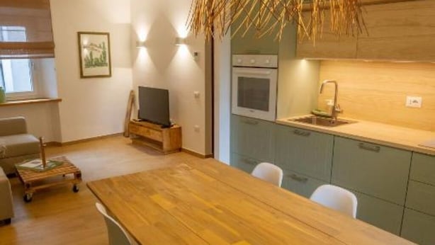 A modern kitchen with a wooden table and chairs, a built-in oven, and a small dining area. - Le Scalette Apartment - G (Osimo)