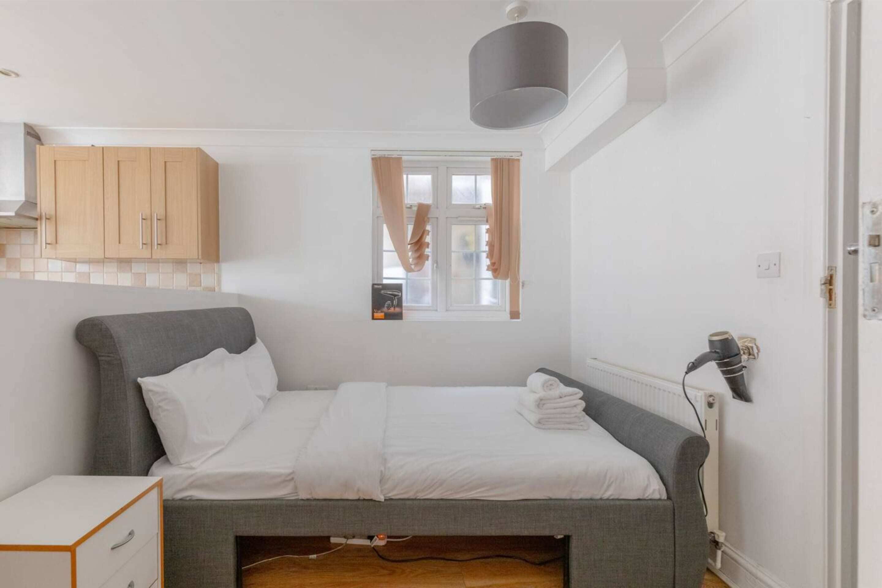 A bedroom with a bed, a nightstand, a wardrobe, a window with curtains, and a radiator.