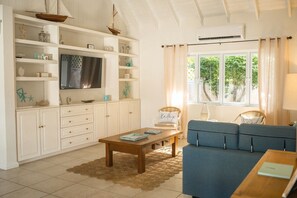 Un salon avec un téléviseur, un canapé, une table basse et une fenêtre avec des rideaux.