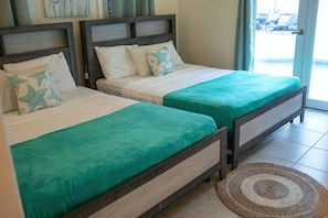 Two twin beds with matching headboards and footboards, a woven mat on the floor, and a view of the outside through a glass door.