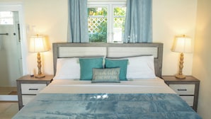 A bed with a blue bedspread, two bedside tables with lamps, and a window with curtains.