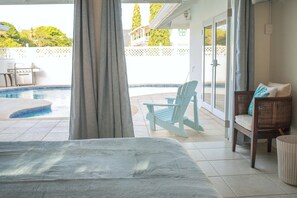A room with a view of a swimming pool, a chair, and a wicker chair with cushions. - The Heart Villa - Sleeps 16, 5BR Heart-Shaped Pool, Gazebo, Play Park (Canaan, Tobago)