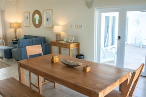 A dining area with a wooden table, chairs, and a bowl. There is a blue sofa and a lamp in the background.