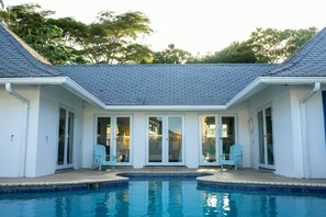 A poolside area with a clear view of the pool, two chairs, and a covered patio with glass doors.
