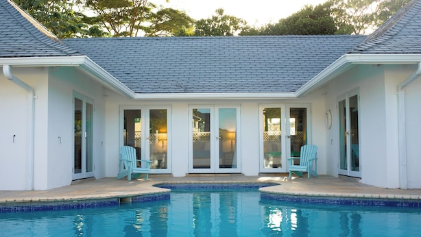 A swimming pool with a tiled edge, surrounded by a covered patio area with two light blue chairs and a table.