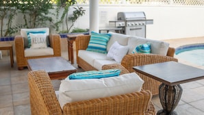 Wicker furniture with cushions, a pool, and a grill in the background.