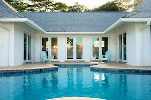 A swimming pool with a covered patio area, two doors, and two chairs.