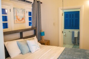 A bedroom with a bed, a nightstand, a lamp, a painting, and a bathroom door. - The Heart Villa - Sleeps 16, 5BR Heart-Shaped Pool, Gazebo, Play Park (Canaan, Tobago)