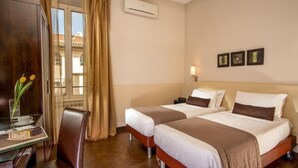 A hotel room with two beds, a desk with a chair, a vase with flowers, and a window with curtains. - Basilio Veneto Rome (Rome)