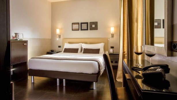 A hotel room with a large bed, bedside tables, a mirror, and a telephone. - Basilio Veneto Rome (Rome)