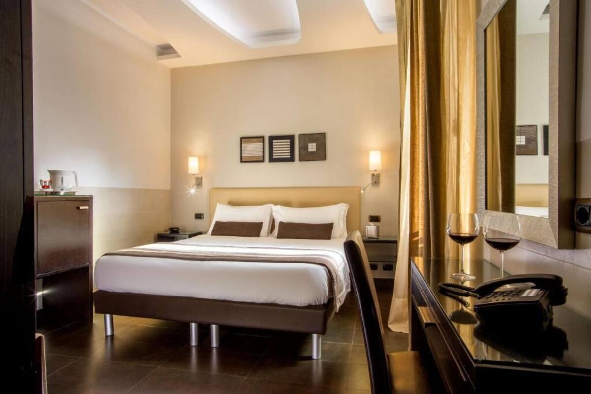 A hotel room with a large bed, bedside tables, a mirror, and a telephone.