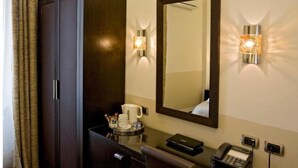 A hotel room with a dark wooden wardrobe, a mirror with wall-mounted lights, a small table with a coffee pot, cups, and a phone. - Basilio Veneto Rome (Rome)