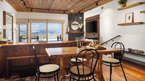 A wooden dining area with a large table and chairs, a television, and a view of mountains through large windows. - Grand Teton View!!! Jackson Hole's Spring Creek Lookout (Jackson)