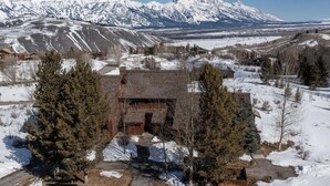 A rustic cabin with a stone foundation and wooden walls, surrounded by snow-covered ground and trees, with a mountain range in the background. - Grand Teton View!!! Jackson Hole's Spring Creek Lookout (Jackson)