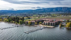 A waterfront hotel with multiple buildings, docked boats, and a view of a city and mountains in the background.