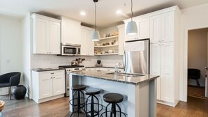 A modern kitchen with white cabinets, a central island with stools, stainless steel appliances, and pendant lighting.