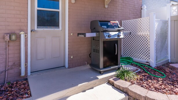 Una parrilla de barbacoa frente a una casa con pared de ladrillo, puerta blanca y valla blanca.