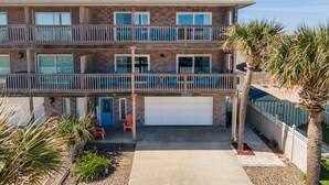 A two-story residential building with a brick facade, a garage, and a front yard with palm trees and a white picket fence. - Private Pool, Ocean View Entire Home in Beautiful New Smyrna Beach, FL. (New Smyrna Beach)