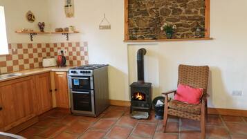 A cozy kitchen with a stone wall, a wood-burning stove, and a chair with a red cushion.