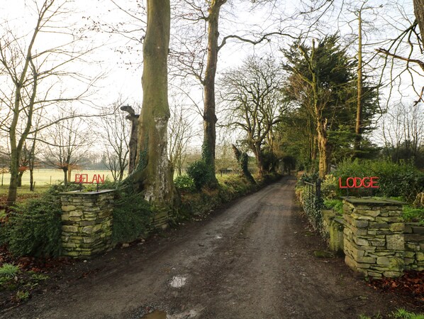 A rural road leading to a stone-built lodge with a sign indicating its name.