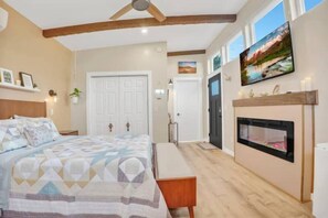 A bedroom with a bed, a bench, a fireplace, and a TV mounted on the wall. - Cozy Guest House Perfect For Couples w/ Hot Tub (Sedona)