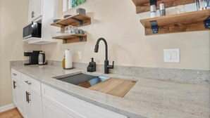 Una cocina con armarios blancos, encimera de granito, grifo negro y estantes de madera.