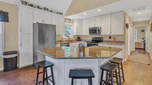 A kitchen with white cabinets, a granite countertop, a stainless steel refrigerator, a microwave, and a large island with stools. - Smith Mountain Lake Waterfront Retreat w/ Hot Tub, Pool Table, & Games (Moneta)
