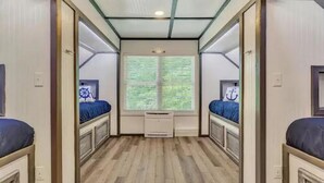 A narrow corridor with two beds on either side, a window with blinds, and a small air conditioning unit in the center. - Smith Mountain Lake Waterfront Retreat w/ Hot Tub, Pool Table, & Games (Moneta)