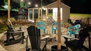 An outdoor patio area with Adirondack chairs, a fire pit, and a covered seating area with string lights. - Smith Mountain Lake Waterfront Retreat w/ Hot Tub, Pool Table, & Games (Moneta)