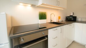 A modern kitchen with white cabinets, a black countertop, stainless steel appliances, and a small indoor plant. - Stylish & Modern Apartment (Vienna)