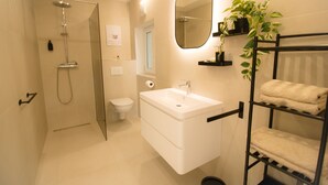 A modern bathroom with a glass-enclosed shower, a white sink, a mirror, and a towel rack with folded towels. - Stylish & Modern Apartment (Vienna)