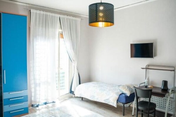 A bedroom with a bed, a desk, a chair, a TV, and a wardrobe.