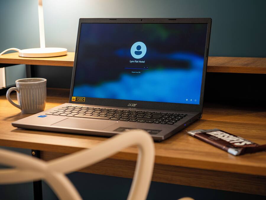 Um laptop sobre uma mesa de madeira, com uma caneca e uma barra de chocolate ao lado.