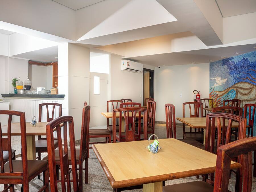 A dining area with wooden tables and chairs, a kitchen in the background, and a colorful mural on the wall.