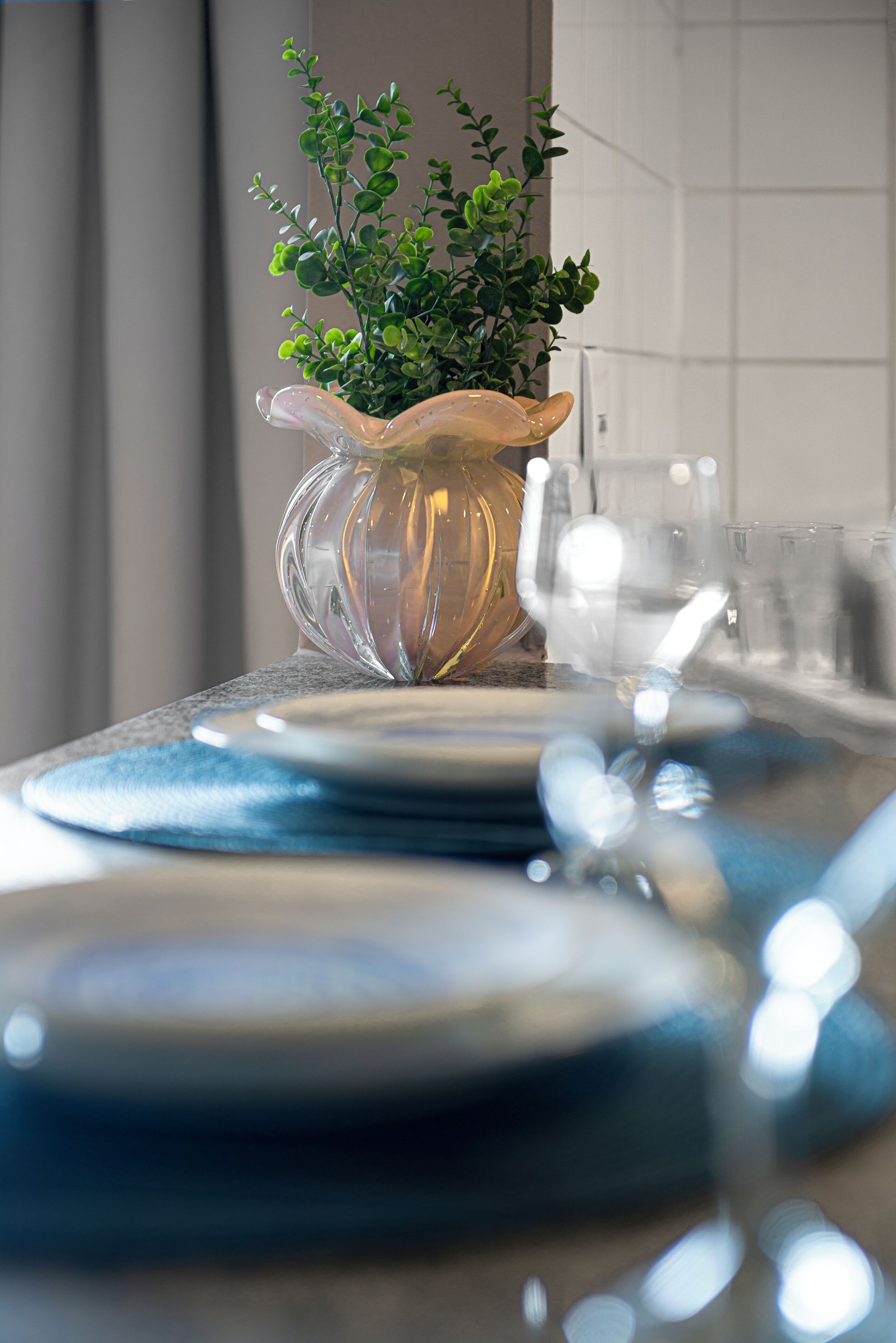 A table set with blue plates, a clear glass pitcher, and a green plant.