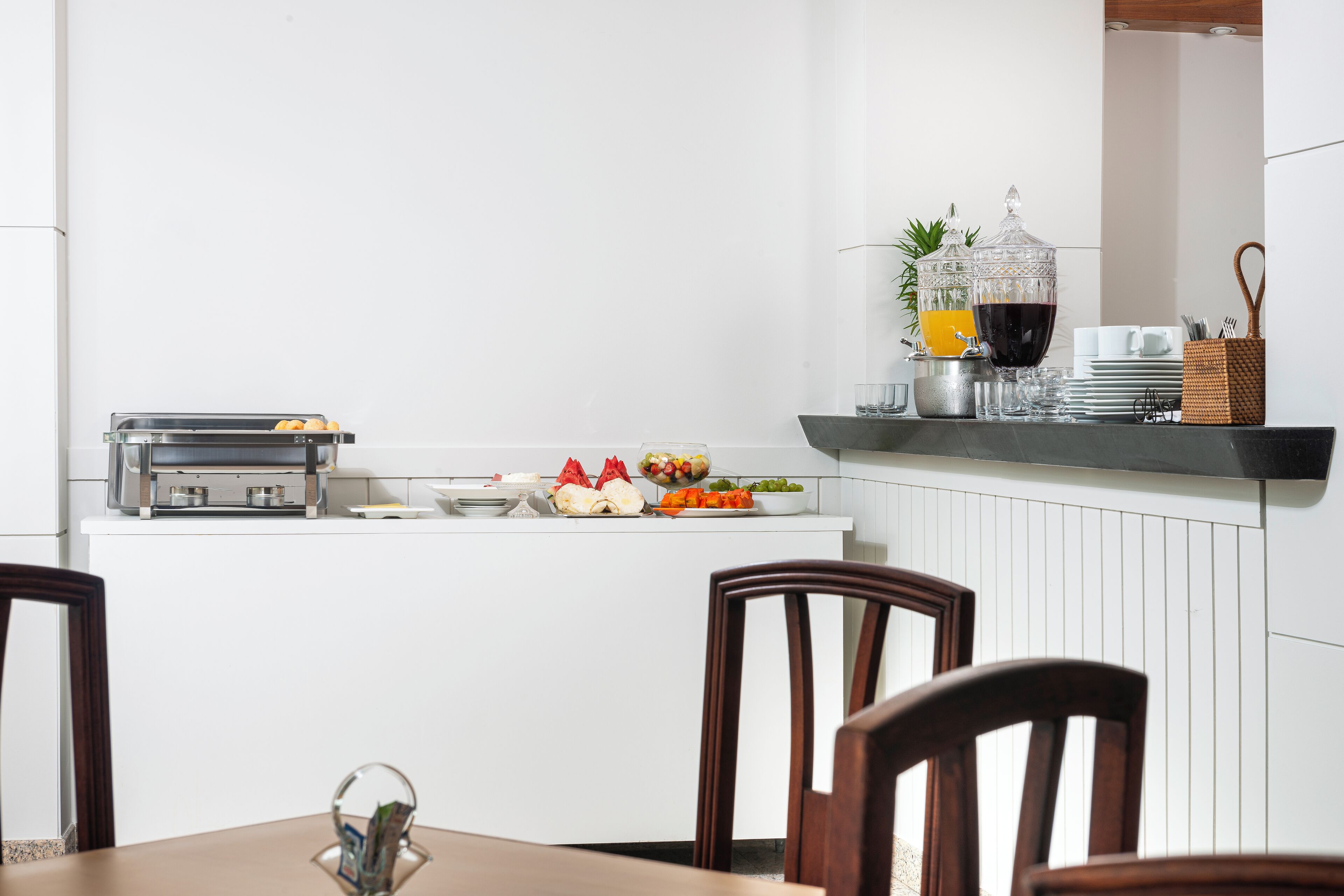 A breakfast bar with a coffee machine, a fruit bowl, and a glass of juice.