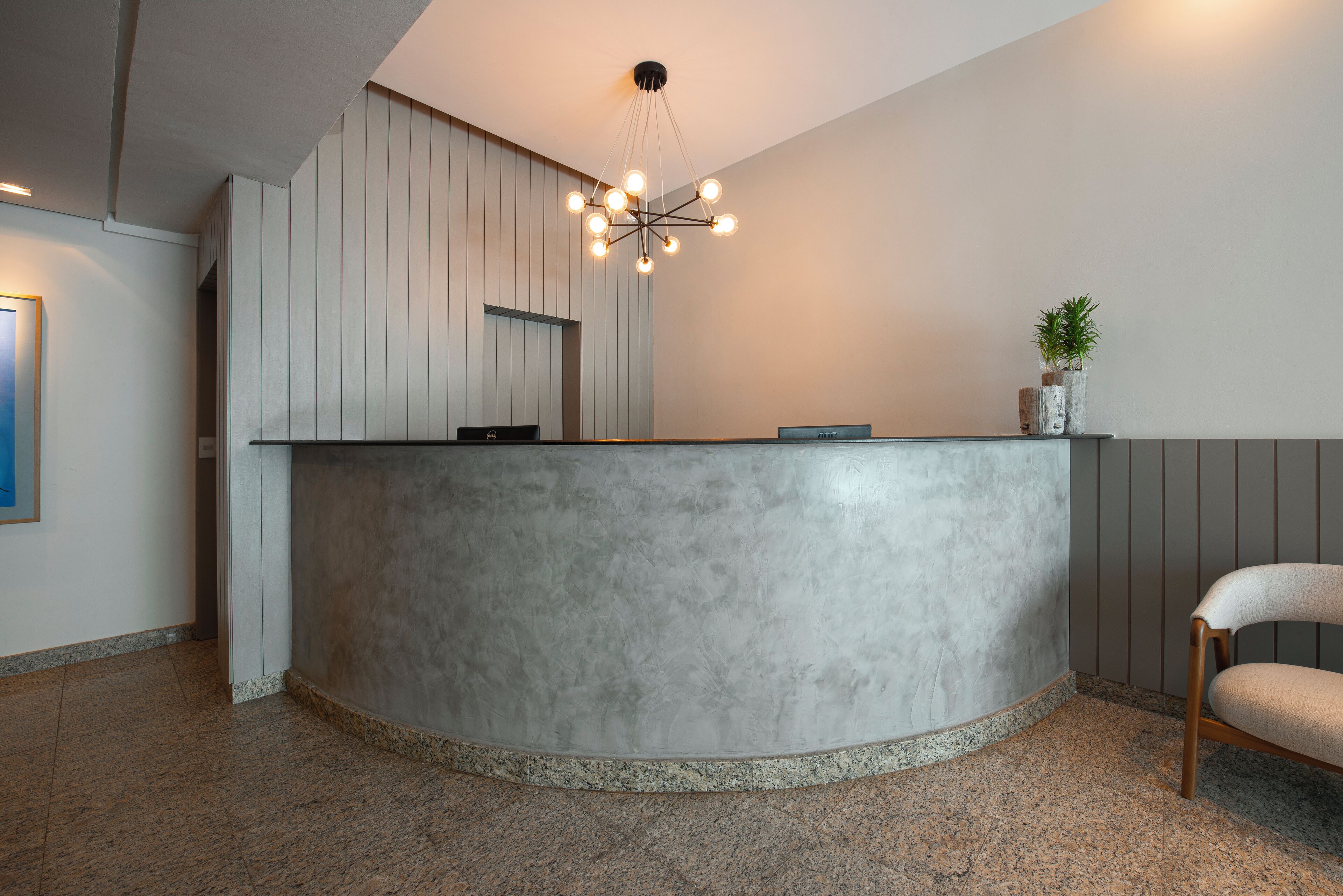 A reception area with a curved grey reception desk, a modern chandelier, and a potted plant.
