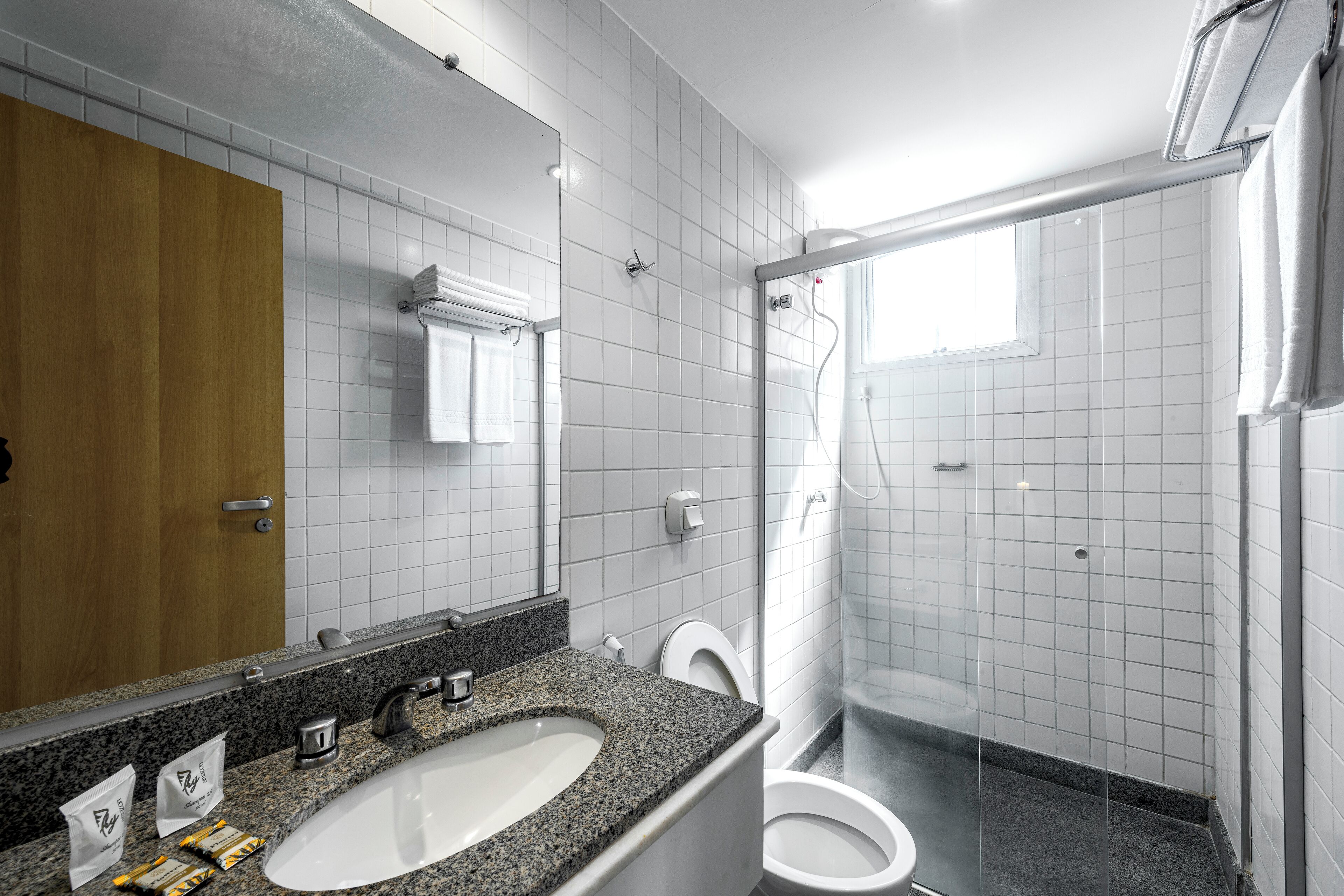 A modern bathroom with a granite countertop sink, a white toilet, and a glass-enclosed shower.